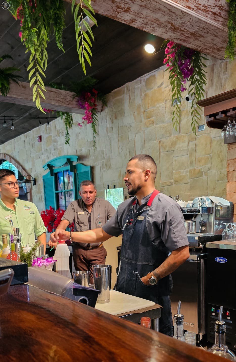 Bartender crafting cocktails at a Caribbean-style bar with stone walls and tropical flowers