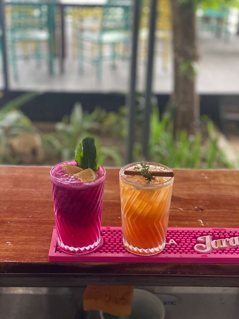 A vivid magenta and an orange cocktail side by side on the bar